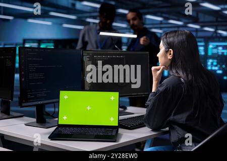 Woman working on laptop with isolated screen monitor in modern data center. IT professional doing IT infrastructure management on server racks in high tech environment using mockup notebook Stock Photo