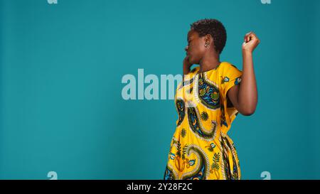 Casual young adult stretching and relaxing in the studio, wearing a traditional attire with floral native elements. Confident cheerful woman straightening her back, fixing her posture. Camera B. Stock Photo