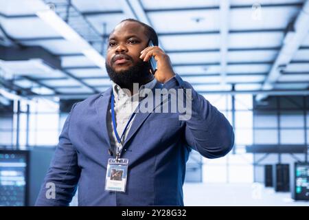 Supervisor discussing on mobile phone in high tech data center housing advanced computing hardware. Professional delegating tasks in futuristic server farm during telephone call Stock Photo