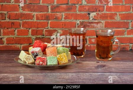 Two transparent glass glasses of hot tea in oriental style and a plate with an assortment of colorful sweets on a wooden table. Close-up. Stock Photo