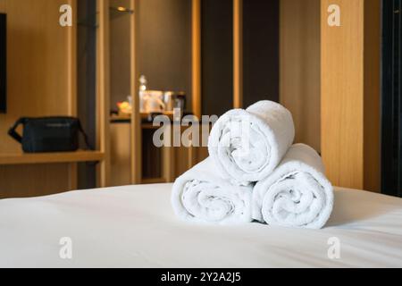 Contemporary hotel room with rolled white bath towels on top of bed. Stock Photo