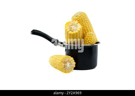 Fresh corn cobs arranged in a black saucepan with additional cobs around Stock Photo