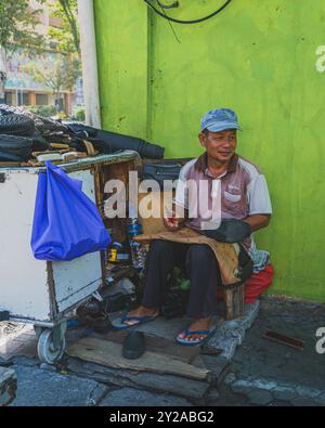 Balikpapan, Indonesia - June 22nd, 2024.  street vendor repairing shoes at an outdoor workshop. The image showcases the cobbler's tools, work in progr Stock Photo