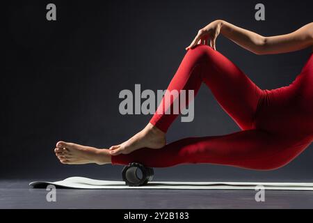 Sporty woman doing body massage with foam roller on mat on black background. Muscle relaxation. Concept of sporty lifestyle, beauty, body and health, Stock Photo