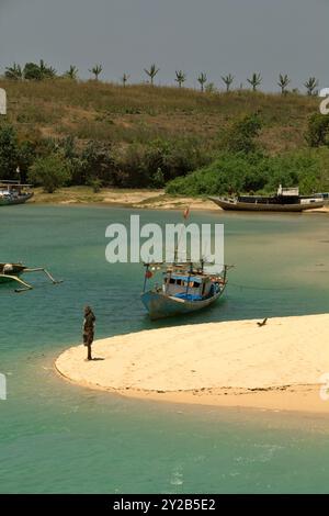 A fisherman standing on sandy beach in a background of fishing boats on a lagoon-like seascape in the fishing beach of Pero in Sumba Island, Indonesia. Stock Photo