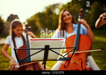 People, instruments and book in nature for music, talent and entertainment for event. Musicians, string trio and smile on grass for art, rehearsal and Stock Photo