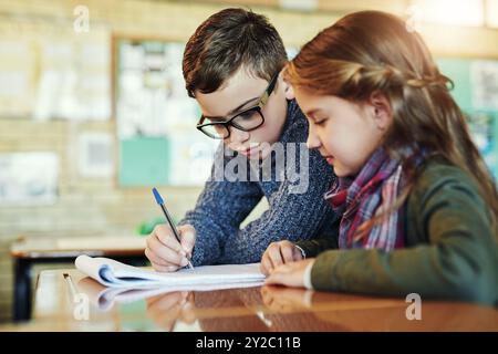 Classmates, kids and writing in classroom for education with learning, knowledge and group work. Pupil, students and serious at elementary school for Stock Photo