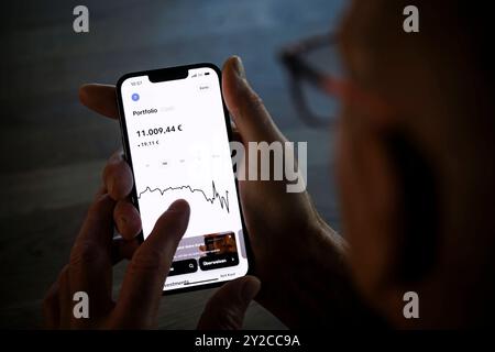 Symbolfoto zum Thema Geldgeschaefte im Alter digital abwickeln. Ein Alter Mann haelt ein Smartphone mit der Trade Republic App und prueft den Aktienku Stock Photo