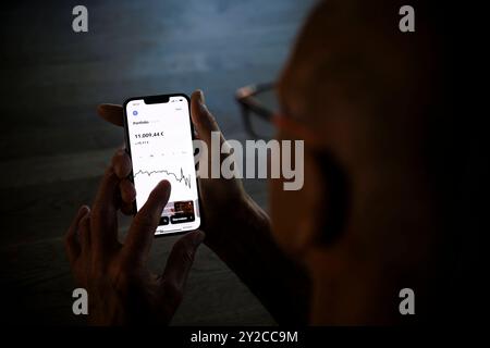 Symbolfoto zum Thema Geldgeschaefte im Alter digital abwickeln. Ein Alter Mann haelt ein Smartphone mit der Trade Republic App und prueft den Aktienku Stock Photo