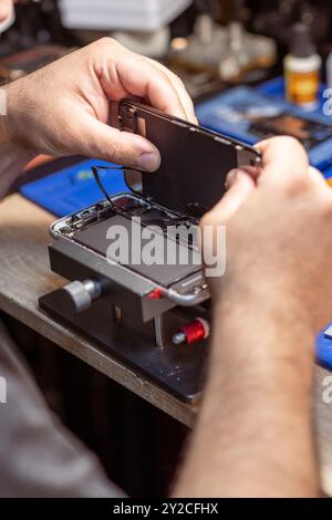 A technician carefully disassembles a smartphone to replace its battery in a well-equipped repair shop Stock Photo