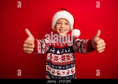 Photo portrait of charming small boy thumb up approve celebrate christmas dressed knitted sweater isolated on red color background Stock Photo