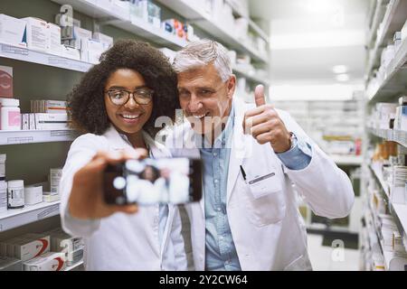 Selfie, people and healthcare in pharmacy, smile and wellness of medicine, store and photography. Thumbs up, lab coat and pharmacist with mature man Stock Photo
