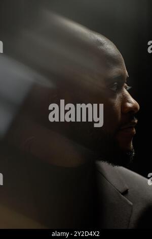 Vertical profile shot of adult African American man in formal suit looking away with expression of grief and sad contemplation lost in memories in low key lighted studio, ghost glare effect Stock Photo