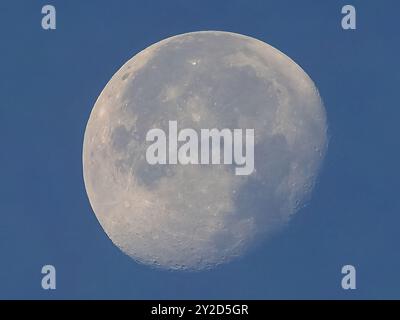 Full moon seen with astronomic telescope over blue sky in the morning Stock Photo