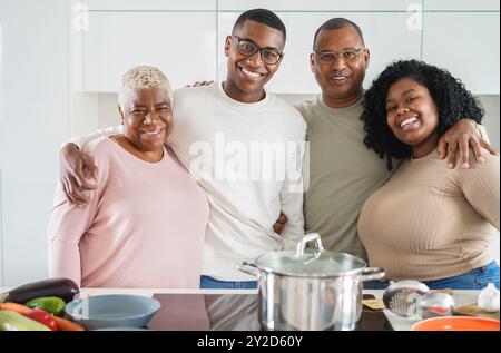 Happy black family cooking inside kitchen at home - Father, daughter, son and mother having fun preparing lunch - Main focus on father face Stock Photo