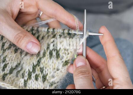 Norwegian knitted pattern in woman hands. Girl holding knitting needles and beautiful knitting pattern. Woman with green and beige knitted pattern. Stock Photo