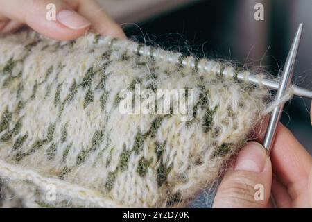 Norwegian knitted pattern in woman hands. Girl holding knitting needles and beautiful knitting pattern. Woman with green and beige knitted pattern. Stock Photo