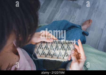 Norwegian knitted pattern in woman hands. Girl holding knitting needles and beautiful knitting pattern. Woman with green and beige knitted pattern. Stock Photo