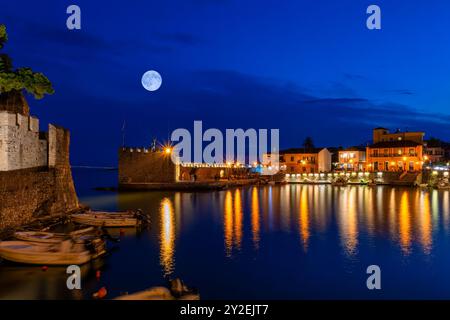 Lights reflecting water at the port of Nafpaktos in Greece against the full moon. Stock Photo