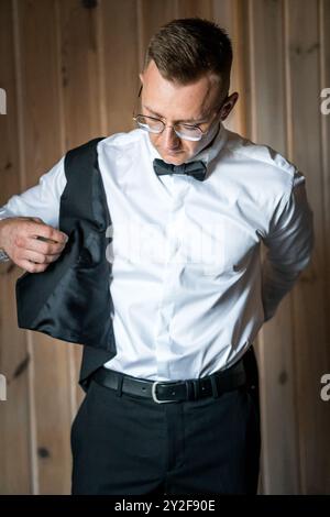 Elegant Man Adjusting Suit Jacket in Stylish Formal Attire Against Wooden Background. Stock Photo