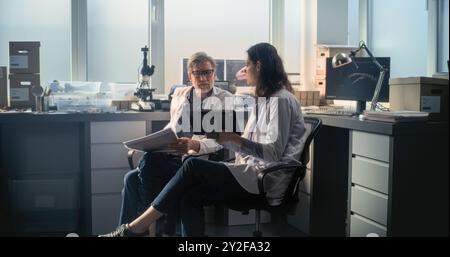 Male and female scientists in lab coats conduct scientific research, use tablet computer and have discussion. Paleontologists or archaeologists work in advanced archaeological lab. Science concept. Stock Photo