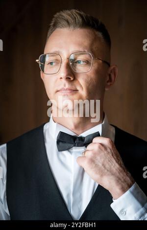 Elegant Young Man in Formal Attire with Glasses and Bowtie in Thoughtful Pose. Stock Photo