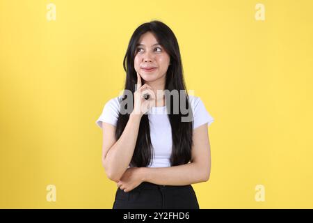 Asian Indonesian Young Woman with Long Hair Doing Thinking Gesture, Isolated on Yellow Background Stock Photo