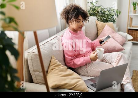 A young woman relaxes at home with coffee while using her phone. Stock Photo