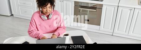 A young woman relaxes while working on her laptop in a stylish kitchen. Stock Photo