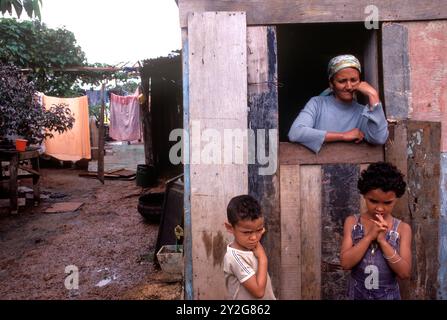 Brazil, the exterior of a favela, a slum house in a poor shanty town, the so called Free City a suburb of Brasilia. Children and their mother outside their wooden shack home. Brasilia Brazil, South America June 1985 1980s HOMER SYKES Stock Photo