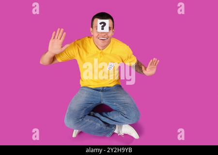 Young man with paper question mark on his forehead against purple background Stock Photo
