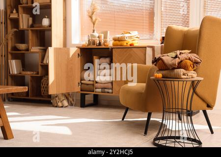 Stack of stylish clothes with autumn decorations on stool near open commode in living room Stock Photo