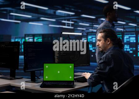 Admin in data center using isolated screen laptop to check for server performance issues. IT specialist in server hub fixing errors slowing down hardware using chroma key notebook Stock Photo