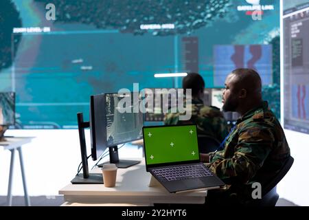 Military IT specialist in command center working on collecting field data, process real time surveillance footage and imagery for successful defense operation. Using isolated mockup display on pc. Stock Photo