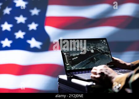 US Air Force officer isolated over USA flag monitoring zone of interest using radar. Close up shot of United States military soldier engaged in surveillance mission using laptop, looking at world map Stock Photo