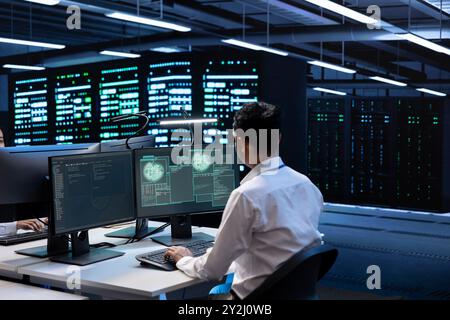 System administrator using computer in server room to support global connections using their hardware. Employee inspecting data center equipment supporting worldwide network using PC Stock Photo