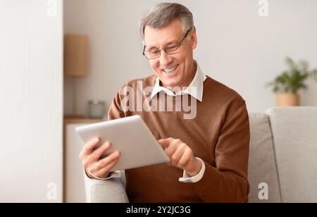 Joyful Retired Man Using Digital Tablet Sitting On Couch Indoor Stock Photo