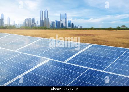 A solar panel is shown on a clear blue sky. The panel is surrounded by a cityscape and a field. Concept of progress and sustainability, as the solar p Stock Photo