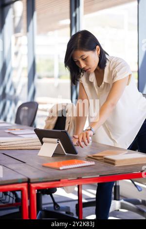 At office, Using tablet, asian woman working on interior design project with samples on table Stock Photo