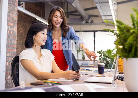 Collaborating on interior design project, diverse women using laptop and smartphone in office Stock Photo