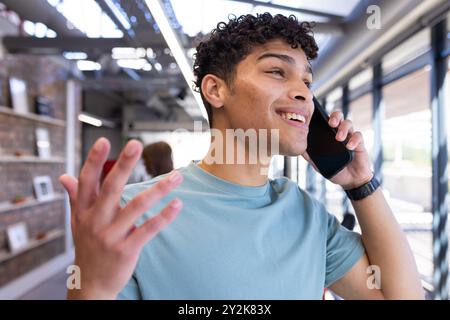 At office, Talking on smartphone, young man smiling and gesturing in modern interior space Stock Photo