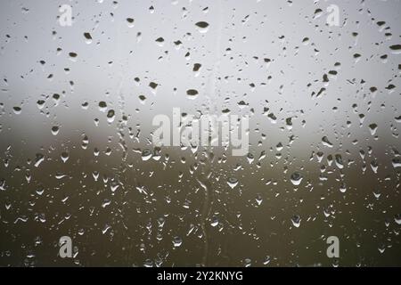 A window with raindrops on it. The raindrops are scattered all over the window, creating a blurry and hazy effect. Scene is calm and peaceful, as the Stock Photo