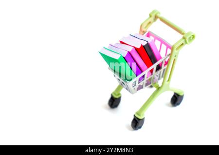 Mini shopping cart filled with brightly colored books, isolated on white background. Education, reading, and consumerism concept. Stock Photo