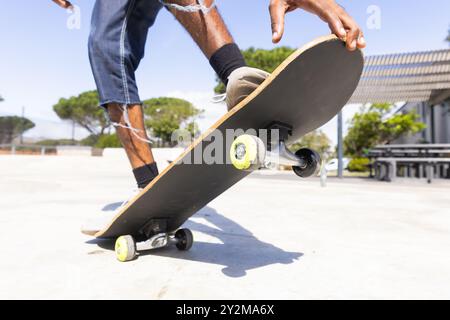 Performing skateboard trick in park, african american teenage boy skateboarding outdoors Stock Photo