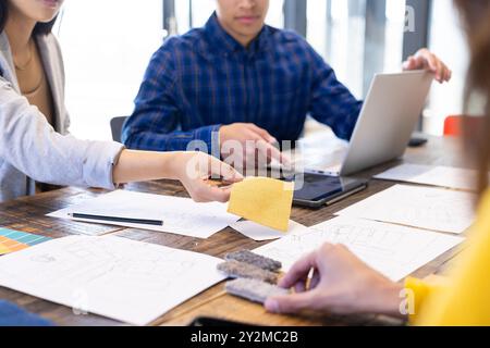 At office, Diverse team collaborating, reviewing fabric samples and blueprints at table Stock Photo
