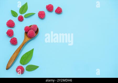 Wooden spoon of ripe raspberries on table, angle view. Three raspberries in one spoon and leaves on a blue wooden table Stock Photo
