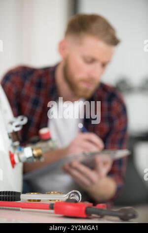 plumber writing in clipboard and checking electric boiler Stock Photo