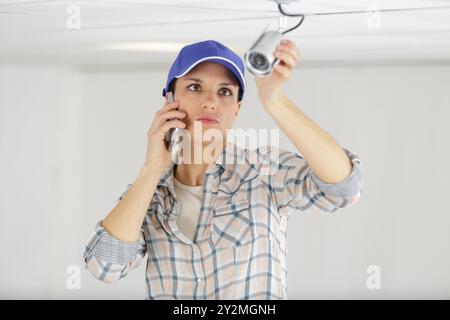 female technician on the phone fitting cctv camera Stock Photo