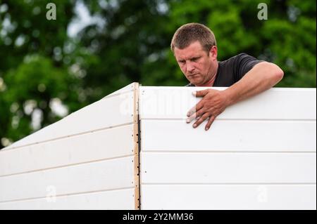 Ivano-Frankivsk, Ukraine, May 10, 2024: A worker screws in a screw and thus fastens two walls of a garden house. Stock Photo