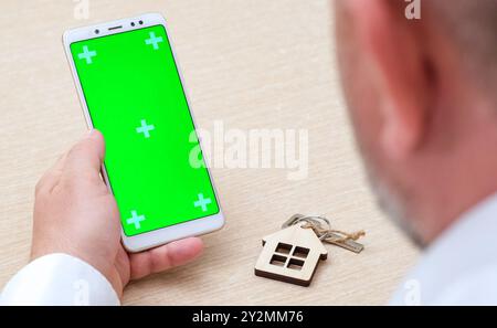 Man using mock up phone in vertical position next to house key. Person with blank smartphone Stock Photo